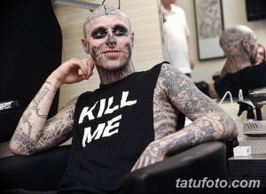 Фото тату: мужчина с татуировкой черепа на лице, в майке с надписью 'Kill Me'. Агрессивный стиль, реалистичный рисунок.